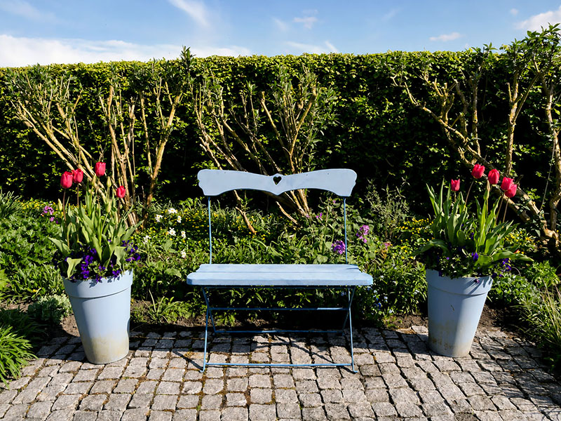 Wit tuinbankje met potten roze tulpen tegen een groene haag